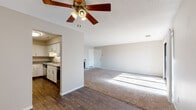 This single-floor residence offers a thoughtfully arranged layout visible across its interconnected living spaces. The main living area is generously sized, featuring plush wall-to-wall carpeting, a ceiling fan with light fixture, and a textured ceiling. A tile-surround fireplace anchors one wall, while a large sliding glass door opens to a private balcony, allowing abundant natural light to fill the room. The adjoining dining or secondary living area shares the same open feel, with hardwood-style flooring transitioning from the kitchen.

The kitchen is efficiently designed with white shaker-style cabinetry, granite-look countertops, stainless steel appliances including a refrigerator and dishwasher, and a single-basin sink. The space is practical and well-lit with under-cabinet lighting.

Two carpeted bedrooms provide comfortable retreats. The primary bedroom includes dual sliding closets and a private en-suite bathroom with a single-sink vanity, stone-look countertop, white cabinetry, and a walk-in shower. The second bedroom features a window with vertical blinds and closet access. A secondary full bathroom offers a tub-shower combination, hardwood-style flooring, and neutral wall tones throughout.
