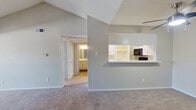 This single-floor, 2-bedroom, 1-bathroom residence offers a well-organized layout with a variety of functional spaces across its footprint. The living room is a standout area, featuring dramatic vaulted ceilings that lend a sense of openness and volume beyond its physical dimensions. A classic fireplace with a dark surround and white mantle serves as a focal point, complemented by neutral carpet flooring and soft gray walls throughout. An adjacent secondary living area extends the space, connected seamlessly to a pass-through kitchen. The kitchen is outfitted with white shaker-style cabinetry, stone-look countertops, and black Whirlpool appliances including a range and over-the-range microwave, with dark hardwood-style flooring adding contrast. The primary bedroom is generously sized, featuring dual windows with horizontal blinds that allow ample natural light and a ceiling fan for comfort. The second bedroom is cozy and well-proportioned with its own window. The full bathroom includes a quartz-topped vanity, tiled shower-tub combo, and wood-style flooring. A dedicated laundry room houses a full-size washer and dryer and includes overhead shelving for additional storage. A closet rounds out the unit's practical storage offerings.