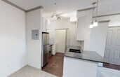 This single-floor unit offers a thoughtfully designed layout that balances functionality with modern finishes throughout. The open-concept kitchen is equipped with stainless steel appliances, including a refrigerator and range, complemented by white cabinetry, a dark granite-style countertop, a subway tile backsplash, and pendant lighting overhead. A raised breakfast bar separates the kitchen from the main living area, which features neutral carpeting and flows naturally toward a set of French doors topped with a transom window, providing outdoor access and filling the space with natural light.

The unit includes two carpeted bedrooms, each outfitted with a ceiling fan and window with exterior views. One bedroom features a direct connection to a full bathroom, while the other provides easy hallway access. The bathroom is finished with dark gray subway tile surrounding a soaking tub and shower combination, a dark granite-topped vanity with an undermount sink, and a large framed mirror. Wood-look flooring anchors the wet areas, adding warmth and contrast.

A dedicated laundry area houses a full-size top-loading washer and dryer with overhead shelving for added storage. The unit also includes a double-door closet near the entryway and a conveniently located electrical panel. Crown molding throughout adds a clean, polished finish to the overall aesthetic.