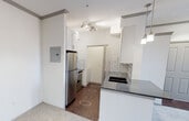 This single-floor unit offers a thoughtfully designed layout that balances functionality with modern finishes throughout. The open-concept kitchen is equipped with stainless steel appliances, including a refrigerator and range, complemented by white cabinetry, a dark granite-style countertop, a subway tile backsplash, and pendant lighting overhead. A raised breakfast bar separates the kitchen from the main living area, which features neutral carpeting and flows naturally toward a set of French doors topped with a transom window, providing outdoor access and filling the space with natural light.

The unit includes two carpeted bedrooms, each outfitted with a ceiling fan and window with exterior views. One bedroom features a direct connection to a full bathroom, while the other provides easy hallway access. The bathroom is finished with dark gray subway tile surrounding a soaking tub and shower combination, a dark granite-topped vanity with an undermount sink, and a large framed mirror. Wood-look flooring anchors the wet areas, adding warmth and contrast.

A dedicated laundry area houses a full-size top-loading washer and dryer with overhead shelving for added storage. The unit also includes a double-door closet near the entryway and a conveniently located electrical panel. Crown molding throughout adds a clean, polished finish to the overall aesthetic.