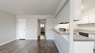 This well-organized 2-bedroom, 1-bathroom single-floor unit offers a practical and cohesive layout with a clean, neutral aesthetic. Dark wood-look flooring runs consistently throughout the space, providing a warm contrast to the crisp white walls and trim found in every room.

The living area is bright and open, featuring a window with blinds that allows natural light to fill the space. It connects seamlessly to the kitchen via a tiled pass-through counter, which also includes a built-in sink and range hood. The kitchen is equipped with white cabinetry, a refrigerator, and an in-unit washer — a convenient and practical feature. A ceiling fan with a light fixture provides additional airflow and illumination.

A central hallway connects the main living areas to the two bedrooms and bathroom. Each bedroom is modestly sized with neutral gray walls, wood-look flooring, and windows fitted with blinds. Both rooms include sliding closet doors, offering practical built-in storage. The primary bedroom provides a quiet, functional retreat.

The bathroom features a full tub-shower combination with white tile surround, a toilet, and a single-sink vanity with white cabinetry. The overall design of the unit prioritizes functionality and simplicity, making it an efficient and move-in-ready living space.