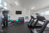 Located at 1785 Almaden Road in San Jose, California, this fitness center offers a thoughtfully designed exercise space on a single floor. The room is finished with clean white walls and durable rubber-speckled flooring suited for high-traffic athletic use. Elevated clerestory windows along multiple walls flood the space with abundant natural light while maintaining privacy, and a wall-mounted mini-split HVAC unit ensures a comfortable workout environment year-round.

The cardio zone is well-appointed with multiple treadmills, elliptical trainers, a stationary upright bike, and a Peloton-style cycling bike, each positioned to allow ample personal space. A large wall-to-wall mirror on one side visually expands the room and supports strength training form, flanking a multi-function cable machine suitable for a wide range of resistance exercises. A dedicated free weights area features a full rack of dumbbells in graduated sizes, a weight bench, stability balls, and additional accessories for functional training. Wall-mounted flat-screen TVs are positioned throughout for entertainment during workouts.

A small utility alcove near the entrance provides a water station and waste disposal, adding convenience to the space. The overall design is modern, clean, and efficient, maximizing every square foot to deliver a comprehensive fitness experience.