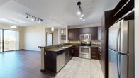 Located at 301 W Jefferson Blvd in Fort Wayne, Indiana, this well-appointed 2-bedroom, 2-bathroom residence offers a thoughtfully designed layout across a single floor. The open-concept kitchen is a standout feature, showcasing rich dark cabinetry, granite countertops, a mosaic tile backsplash, and a full suite of stainless steel appliances including a refrigerator, electric range, and built-in microwave. A peninsula with bar seating and pendant lighting connects the kitchen to the living area, which features hardwood-style flooring and open shelving. The primary bedroom is generously sized, with hardwood-style flooring, a ceiling fan, and floor-to-ceiling sliding glass doors opening to a private balcony with views of the Fort Wayne skyline and surrounding greenery. The second bedroom features plush carpeting, a ceiling fan, and a large window that fills the room with natural light. Both bathrooms are finished with granite-topped dark vanities and tile flooring; one includes a full tub-shower combination. A dedicated closet provides additional storage. The unit balances contemporary finishes with a comfortable, functional layout throughout.