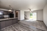 This two-story home offers a thoughtful layout across two floors, providing comfortable living space for everyday life. The main floor features an open-concept kitchen and living area, where wood-look vinyl plank flooring flows throughout. The kitchen is well-appointed with dark cabinetry, a stainless steel range, a refrigerator, a built-in microwave, and a peninsula with a light stone countertop and pendant lighting overhead — ideal for casual dining or meal prep. The living room is bright and airy, with a ceiling fan, a sliding glass door that opens to an outdoor view of green space, and vertical blinds for light control. A carpeted staircase leads to the upper floor, where all three bedrooms are located. The primary bedroom is a comfortable size, while the two additional bedrooms each feature plush carpeting, neutral walls, textured ceilings, and windows overlooking the neighborhood. The two bathrooms include one with a full tub-shower combo and wood-look flooring, and another with a vanity featuring a stone-topped dark cabinet and wood-look flooring. A dedicated laundry room on the upper level houses a full-size washer and dryer with overhead wire shelving. A hallway and closet round out the upper floor, offering practical storage solutions throughout.