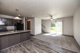 This two-story home offers a thoughtful layout across two floors, providing comfortable living space for everyday life. The main floor features an open-concept kitchen and living area, where wood-look vinyl plank flooring flows throughout. The kitchen is well-appointed with dark cabinetry, a stainless steel range, a refrigerator, a built-in microwave, and a peninsula with a light stone countertop and pendant lighting overhead — ideal for casual dining or meal prep. The living room is bright and airy, with a ceiling fan, a sliding glass door that opens to an outdoor view of green space, and vertical blinds for light control. A carpeted staircase leads to the upper floor, where all three bedrooms are located. The primary bedroom is a comfortable size, while the two additional bedrooms each feature plush carpeting, neutral walls, textured ceilings, and windows overlooking the neighborhood. The two bathrooms include one with a full tub-shower combo and wood-look flooring, and another with a vanity featuring a stone-topped dark cabinet and wood-look flooring. A dedicated laundry room on the upper level houses a full-size washer and dryer with overhead wire shelving. A hallway and closet round out the upper floor, offering practical storage solutions throughout.