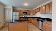 This three-floor residence offers a thoughtfully designed layout with functional and consistent finishes throughout. The kitchens are a standout feature, appearing on multiple levels and showcasing warm honey-toned wood cabinetry with raised-panel detailing that extends to the ceiling for ample storage. Dark granite countertops provide a rich contrast, while a full suite of stainless steel appliances — including a gas range, built-in microwave, refrigerator, and dishwasher — ensures a well-equipped cooking space. Light ceramic tile flooring completes each kitchen's practical design.

The living and bedroom areas are finished with neutral-toned wall-to-wall carpeting that lends a comfortable, quiet atmosphere. Rooms are generously proportioned with clean white walls and six-panel interior doors, contributing to a bright and open feel. Staircase access connects the floors, with the upper level featuring multiple doorways leading to distinct rooms and closet spaces.

Bathrooms are finished with tile flooring and include chrome fixtures. One bathroom features a full tub and shower surround, while another offers a compact half-bath configuration with a pedestal sink and toilet. Overall, the space presents a clean, move-in-ready environment with consistent finishes across all three levels.