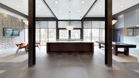 This single-floor clubhouse is designed with a sophisticated contemporary aesthetic, blending functionality and style throughout its open, flowing layout. The grand entry features floor-to-ceiling glass double doors framed in dark steel, flooding the space with natural light and offering views into the community beyond. An eye-catching sputnik-style chandelier marks the entryway, setting an elevated tone from the moment of arrival.

The main gathering area centers around a substantial dark wood island topped with light stone, illuminated by a sculptural globe chandelier. Large-format tile flooring extends throughout, while floor-to-ceiling roller shades line expansive windows, offering flexible control over natural light.

Multiple lounge areas are thoughtfully arranged to encourage both social interaction and relaxed retreat. Plush patterned sofas and rounded upholstered chairs surround wooden coffee tables, with wall-mounted televisions and curated artwork providing visual interest. A dedicated game area features a billiards table set against a boldly designed accent wall finished in layered blue, white, and wood paneling.

Dark structural columns contrast with crisp white walls and warm wood accents throughout, contributing to the space's modern-industrial character. Distinctive cloud-like pendant chandeliers are repeated across zones, unifying the design. The overall ambiance is polished, welcoming, and well-appointed for community gatherings and everyday leisure.