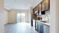 This single-floor unit at 6916 Fulton St in San Diego's Linda Vista neighborhood presents a clean, modern aesthetic throughout its open-concept layout. Light wood-style flooring runs continuously across the living and kitchen areas, complementing neutral warm-beige walls and white trim for a cohesive, contemporary feel.

The kitchen is well-appointed with rich dark espresso cabinetry offering generous upper and lower storage, light-toned countertops, and a full suite of stainless steel appliances including a refrigerator, electric range, over-the-range microwave, and dishwasher. Recessed lighting illuminates the space efficiently.

The living area is generously proportioned and open, bathed in natural light through a sliding glass door that provides outdoor views and access. Vertical blinds offer privacy control. The open sightlines between the kitchen and living space create an inviting, functional flow ideal for daily living.

A dedicated bedroom features the same light flooring and neutral walls, with recessed lighting and ample wall space. The bathroom is finished with matching flooring, clean white walls, and basic fixtures. A utility panel is conveniently positioned along the main corridor. Overall, the unit presents a move-in-ready, well-maintained interior with a bright and practical design.