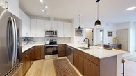 This well-appointed residence in Farmington, MN offers a thoughtfully designed single-floor layout with one bedroom, three bathrooms, and a generous sense of space throughout. The open-concept kitchen and living area serves as the heart of the home, showcasing a two-tone cabinetry design with rich walnut lower cabinets and crisp white uppers, complemented by quartz countertops, a subway tile backsplash, and stainless steel appliances. A large island with seating and stylish pendant lighting makes this space ideal for both everyday living and entertaining. Light hardwood flooring flows seamlessly throughout the entire residence, enhancing its bright, contemporary feel. The living area benefits from a floor-to-ceiling sliding glass door that fills the space with natural light and provides direct access to a private patio. The spacious bedroom features a large window with outdoor views and connects to ample closet space. The bathrooms are finished with matching walnut vanities, white quartz countertops, and matte black fixtures — one featuring a dual-sink vanity with a tub-shower combination. A dedicated in-unit laundry closet with stacked washer and dryer adds everyday convenience, while a utility room rounds out the functional layout of this modern residence.