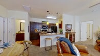 This single-story residence offers a functional and comfortable layout across two bedrooms and two bathrooms. The open-concept living and kitchen area forms the heart of the home, where the kitchen stands out with rich dark-wood cabinetry, granite-style countertops, a large island with a double sink, and bold pendant lighting in amber tones. Black appliances and hardwood-style flooring complete the kitchen's polished look. The living room flows naturally from the kitchen, featuring plush carpet, ceiling fan with light, and multiple windows that allow natural light to fill the space.

The primary bedroom is generously sized with carpeted flooring, a ceiling fan, a walk-in closet, and a window providing natural light. The second bedroom mirrors this comfortable layout. Both bathrooms feature dark wood vanities with stone-style countertops, framed mirrors, and tub-shower combinations with hardwood-style flooring.

A dedicated laundry room with full-size side-by-side washer and dryer adds everyday convenience. Two closets provide ample storage throughout. The overall design maintains a cohesive, warm aesthetic with consistent finishes across all rooms.