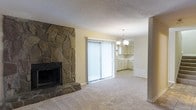 This two-floor residence offers a welcoming and functional layout designed for comfortable everyday living. The main living area is anchored by a dramatic floor-to-ceiling stone fireplace, adding a rustic yet timeless character to the space. Neutral carpet flooring and light-toned walls create a bright, airy atmosphere throughout. A sliding glass door floods the living room with natural light and provides direct access to the outdoors, enhancing the sense of openness.

The living space flows naturally into the kitchen and dining area, where a classic chandelier adds a touch of elegance overhead. The kitchen features light-toned cabinetry with ample storage, offering a clean and practical workspace. The open sightlines between the living room and kitchen make the main floor feel connected and spacious, ideal for both daily routines and entertaining.

A textured ceiling adds subtle visual depth, while the consistent color palette throughout maintains a cohesive and inviting ambiance. With two floors, the residence provides generous room for living, sleeping, and storage, offering a well-rounded layout that balances shared spaces with private retreats.
