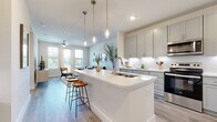 This single-floor residence offers a thoughtfully designed open-concept layout with modern finishes throughout. Light gray luxury vinyl plank flooring runs continuously across the living areas, creating a cohesive and clean aesthetic.

The kitchen serves as a central hub, featuring gray shaker-style cabinetry, white quartz countertops, under-cabinet lighting, and stainless steel appliances including a refrigerator, range, microwave, and dishwasher. A large island with an integrated sink and seating for two provides both prep space and casual dining. Pendant lighting in brushed brass tones hangs above the island, adding a warm contrast to the cool palette. Built-in open shelving adjacent to the kitchen offers additional display and storage space.

The living room is bright and welcoming, with large windows and a glass-paneled door that invite natural light and outdoor views. A ceiling fan with integrated lighting adds practical comfort.

The bedrooms are serene and well-proportioned, each featuring large windows, ceiling fans, and soft neutral tones that promote a restful atmosphere.

The bathroom is finished with a gray vanity, white quartz countertop, a framed mirror with upper cabinetry, and wood-look flooring. A dedicated in-unit laundry room with a full-size washer and dryer and overhead shelving completes this well-appointed residence.
