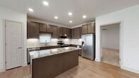 This well-designed single-floor residence offers a thoughtfully laid-out open floor plan with modern finishes throughout. The kitchen serves as the heart of the home, showcasing rich dark cabinetry, granite countertops with subtle veining, a subway tile backsplash, and a full suite of stainless steel appliances including a French door refrigerator, electric range with microwave, and dishwasher. A central island provides additional prep space and casual seating. Recessed lighting and under-cabinet lighting enhance the kitchen's functionality and ambiance.

The living area flows seamlessly from the kitchen and features light wood-look flooring, a ceiling fan, and a bank of windows that invite abundant natural light. A built-in shelving unit along one wall offers practical display and storage space.

The bedrooms are finished with plush carpeting, ceiling fans, and well-sized windows. The primary suite connects directly to a private bathroom equipped with a granite-topped vanity, dark wood cabinetry, a large framed mirror, and a glass-enclosed walk-in shower with white tile surround. An adjacent walk-in closet with built-in shelving and hanging rods completes the suite. Additional carpeted bedrooms provide comfortable, versatile spaces throughout the residence.