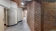 This striking industrial loft blends raw architectural character with modern finishes across a generously sized single-floor layout encompassing 3 bedrooms, 2 bathrooms, an office, dedicated laundry, and open-concept living and dining areas. Soaring wood beam ceilings with exposed ductwork set the tone throughout, complemented by polished concrete floors and prominent exposed brick walls that lend authentic urban character to every room. The open-plan kitchen, dining, and living area is a standout, featuring warm cherry wood cabinetry, granite countertops, stainless steel appliances including a refrigerator, range, microwave, and dishwasher, and a large kitchen island with bar seating. Large windows flood the living space with natural light, while ceiling fans and track lighting add to the functional aesthetic. The hallway corridor showcases bold brick columns and glass block accents, connecting the bedrooms — each with exposed brick feature walls, wood beam ceilings, and abundant natural light. The bathrooms offer a clean, modern design with slate tile flooring, a walk-in shower, and contemporary vanities. A dedicated laundry room and two closets provide practical storage. This loft delivers a compelling combination of industrial heritage and contemporary livability.