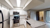 Located at 4600 University Drive in Durham, NC, this single-floor residence offers a thoughtfully designed open-concept layout that seamlessly connects the kitchen and living areas. The kitchen is a standout feature, equipped with stainless steel appliances including a refrigerator, electric range, and built-in microwave, all complemented by crisp white shaker cabinetry, a classic subway tile backsplash, and granite countertops that extend to a peninsula with an undermount sink. Light wood-style flooring runs throughout the main living spaces, contributing to a clean, contemporary aesthetic. The spacious living area is bathed in natural light, with sliding glass doors opening to a private patio that overlooks lush greenery, creating a seamless indoor-outdoor connection. An in-unit laundry area adds everyday convenience. The bathroom features a granite-topped vanity with a large mirror, light wood flooring, and a shower-tub combination. A generously sized walk-in closet offers extensive wire shelving and built-in basket organizers, providing ample storage. Neutral wall tones and consistent modern finishes throughout contribute to a cohesive and inviting atmosphere.