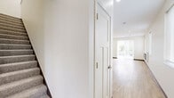 This two-story home in Rochester, Minnesota offers four bedrooms and three bathrooms across a well-designed layout spread over two floors. The main floor hosts the larger share of the living space, anchored by an open-concept kitchen and living room. The kitchen is outfitted with white shaker cabinetry, a large center island with a clean quartz-style countertop, stainless steel appliances including a refrigerator, range, microwave, and dishwasher, and striking sculptural pendant lights over the island. Light hardwood-style flooring runs throughout the main level, adding warmth to the bright, neutral palette. The living room features a sleek, wall-mounted linear fireplace flanked by windows that invite natural light. A sliding glass door opens to outdoor views of the surrounding neighborhood. The bedrooms are carpeted and finished with crisp white walls and dark baseboards; several feature vaulted or elevated ceilings, adding a sense of openness. The primary bedroom offers a generous footprint with dual windows. The three bathrooms are cleanly finished with hardwood-style flooring, white vanities with brushed gold hardware, and tub-shower combinations. A staircase connects the two floors, complemented by a hallway and closet for added storage and functionality.