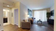 This single-floor residence offers a thoughtfully designed layout that balances comfort and functionality across its main living areas. The living room serves as the heart of the home, featuring warm hardwood-style flooring, a large sliding glass door with vertical blinds that invites abundant natural light, and ample space for relaxed seating arrangements. A dedicated dining area adjacent to the living space includes pendant lighting overhead and hardwood-style flooring that continues the cohesive aesthetic throughout. The kitchen is outfitted with rich dark cabinetry, granite-style countertops, stainless steel appliances including a range and built-in microwave, and light tile flooring — providing both style and practicality. The primary bedroom offers plush carpeting, a generously sized closet with built-in organization, and warm ambient lighting. The second bedroom, also carpeted, features multiple windows that bring in natural light, making it a comfortable and versatile space. Both bathrooms are finished with tile flooring, dark vanity cabinetry with granite-style countertops, and a shower-tub combination. The overall aesthetic is clean and contemporary, with neutral warm tones, consistent finishes, and a welcoming ambiance throughout.