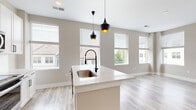 This well-appointed single-floor residence offers a thoughtfully designed layout comprising one bedroom, one bathroom, a kitchen, and a dedicated closet. The open-concept kitchen serves as the centerpiece of the home, featuring crisp white shaker cabinetry, a quartz waterfall island with an undermount sink and matte black gooseneck faucet, a classic white subway tile backsplash, and stainless steel appliances. Striking black pendant lights hang above the island, adding a modern contrast to the bright, neutral palette. Multiple windows flood the kitchen and living area with natural light, offering views of the surrounding neighborhood. Light wood-look flooring extends throughout the main living spaces, lending warmth and continuity. The bedroom is carpeted for comfort and includes a ceiling fan and a walk-in closet with built-in shelving and hanging rods. The full bathroom is elegantly finished with a white double vanity topped with quartz countertops, a large framed mirror, matte black fixtures, and a shower-tub combination. A hallway with paneled white doors and recessed lighting connects all rooms, completing this clean, contemporary residence.