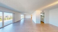 This single-floor residence offers a clean, modern aesthetic defined by light-toned wood-style flooring, crisp white walls, and textured ceilings throughout. The expansive open-plan living and dining area is one of the unit's most notable features, providing generous room to arrange living and dining spaces while benefiting from abundant natural light streaming through large sliding glass doors. These doors open to outdoor views that include water and surrounding buildings, lending the space a bright, airy quality.

The galley-style kitchen is efficiently designed with white shaker cabinetry, light stone countertops, a mosaic tile backsplash, and a full suite of stainless steel appliances including a refrigerator, electric range, microwave, and dishwasher. Recessed lighting ensures the kitchen remains well-illuminated.

The bedrooms are generously proportioned, with one featuring its own sliding glass door with outdoor access and views, while another includes mirrored sliding closet doors for added storage. Both rooms carry the same consistent wood-style flooring found throughout the unit.

The bathrooms include a full bath with a soaking tub and tiled shower surround, and a secondary bath with a white vanity, large mirror, and contemporary lighting. The overall ambiance is clean, neutral, and move-in ready.