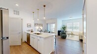 Located at 5155 Raglan St. in Hilliard, Ohio, this one-bedroom, one-bathroom residence offers a smart and stylish layout that maximizes every square foot of its single-floor footprint. The open-concept kitchen and living area serves as the heart of the home, featuring crisp white cabinetry, stainless steel appliances, and a generous island with a built-in sink and seating for multiple bar stools. Pendant lighting with gold brass fixtures adds a refined touch overhead, while light wood-style flooring flows throughout, lending warmth and continuity to the space. The living area is bathed in natural light from a large window with plantation shutters, creating an inviting and airy atmosphere. The bedroom is a comfortable retreat, finished with plush carpeting and a bright window that frames outdoor views. A dedicated walk-in closet offers ample wire shelving and storage space. The full bathroom includes a soaking tub and shower combination with built-in shelving, complemented by clean, bright finishes. A separate laundry area adds everyday convenience. Throughout the residence, tall ceilings, neutral tones, and consistent design elements create a cohesive and modern living environment.