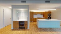 This contemporary single-floor residence offers a thoughtfully designed open-concept layout finished with warm light hardwood flooring throughout the main living areas. The expansive living space is defined by large black-framed windows on multiple walls, flooding the interior with natural light and framing striking panoramic city skyline views. A concrete structural column adds an industrial architectural accent to the open living area.

The kitchen is a standout feature, equipped with rich natural wood cabinetry, a sleek white quartz island with an integrated sink, a cooktop, double stainless steel wall ovens, and a built-in wine refrigerator. A wet bar area with glass shelving and an additional sink provides an elegant entertaining station adjacent to the main kitchen.

A wide hallway connects the living areas to the private rooms, with a plush-carpeted bedroom that opens directly to the kitchen and living spaces. The primary bathroom is finished with large-format dark stone-effect tiles, a deep soaking tub, a floating wood vanity with a white countertop, and a backlit vertical mirror. A separate water closet with neutral tile flooring provides added privacy and convenience. The overall aesthetic is clean, modern, and sophisticated, with a neutral palette throughout.