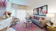 This single-floor residence offers a thoughtfully designed open layout that connects the key living spaces seamlessly. The kitchen is a functional standout, outfitted with crisp white shaker cabinetry, light stone countertops, stainless steel appliances including a refrigerator, range, and microwave, and light wood-style flooring that extends throughout the main living areas. Generous upper cabinet storage, including space above the cabinets for additional organization, adds to the kitchen's practicality.

The living room is bright and welcoming, benefiting from large sliding glass doors dressed with sheer white curtains that allow ample natural light to fill the space. A dedicated dining area features a round wood table and adjoins a built-in desk nook with white cabinetry and under-cabinet lighting, offering a convenient workspace.

The bedrooms are finished with plush carpet flooring and feature windows with blinds and curtains, providing a calm and restful atmosphere. Closet space is available in the bedrooms for convenient storage.

The bathroom is clean and simply appointed, featuring a full soaking tub with a tiled surround and light wood-style flooring that complements the rest of the residence. Throughout the space, a neutral white color palette creates a bright, airy ambiance well-suited for modern living.