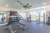 Located at 8146–8162 Shore Dr in Norfolk, Virginia, this single-story fitness center is designed to provide a comprehensive workout experience in a bright, well-appointed environment. The space is divided into distinct exercise zones, each thoughtfully equipped to support a full range of fitness activities.

The cardio area features multiple treadmills, elliptical machines, and a stationary bike, all positioned beneath wall-mounted flat-screen televisions for entertainment during workouts. Large mirrors line the walls, enhancing the sense of space and allowing users to monitor their form. Rubber flooring throughout ensures safety and comfort underfoot.

A dedicated strength training zone includes cable and weight machines from Matrix, a multi-function cable station, and an adjustable bench, positioned beside a dramatic floor-to-ceiling window wall that floods the area with natural light and offers views of the surrounding landscape. An additional free weights section provides a full dumbbell rack alongside adjustable benches and built-in open shelving for storage.

The facility also includes a glass-enclosed area — likely a restroom or utility room — a ceiling fan for air circulation, and recessed lighting throughout. The clean, neutral color palette and modern finishes create a focused, energizing atmosphere well-suited for daily fitness routines.