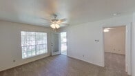 This single-floor unit offers a practical and well-organized layout that makes efficient use of its space. The living area is a standout feature, filled with natural light courtesy of a large picture window and a glass-panel exterior door that opens to an outdoor balcony. Plush carpeting covers the floor, and a ceiling fan with an integrated light fixture provides both comfort and illumination. A textured ceiling adds a classic touch to the room's overall aesthetic. The living space flows seamlessly into the dining and kitchen area, where warm honey-toned wood cabinetry lines the walls, offering generous storage. The kitchen is equipped with black appliances including an electric range, an overhead exhaust hood, and a refrigerator, complemented by light countertops and a double-basin stainless steel sink with durable vinyl plank flooring underfoot. The bedroom continues the carpeted aesthetic and includes a ceiling fan, with direct access to both a full bathroom and the kitchen. The bathroom features a single-sink vanity with a wide mirror, a medicine cabinet, a lighted vanity bar, and a full shower-tub combination. Throughout the unit, clean white walls and consistent finishes create a cohesive and functional living environment.