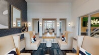 Located at 2429 Americana Blvd in Orlando, FL, this contemporary residential clubhouse is designed to impress with a sophisticated blend of modern aesthetics and functional amenity spaces. The grand lobby welcomes visitors with soaring double-height ceilings, floor-to-ceiling windows, and an abundance of natural light. Cream-toned high-back lounge chairs, bold geometric-patterned area rugs, and textured mosaic accent walls adorned with framed artwork set an upscale tone from the moment you enter.

The main social area features a full-size billiard table anchored beneath dramatic two-story windows that frame views of the outdoor pool and palm-lined courtyard. A tufted banquette in deep gray lines one wall, providing comfortable seating alongside bistro-style tables for casual gatherings. Light wood-style flooring flows throughout, lending warmth and continuity across the space.

A dedicated co-working and dining area offers a long communal table beneath a sculptural chandelier, complemented by abstract artwork and intimate café-style seating nooks. The coffee bar station is equipped with a built-in sink, modern cabinetry, a wall-mounted TV, and a coffee machine, providing a convenient self-serve refreshment hub. A leasing office with glass-paneled doors completes this well-appointed community space.