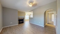 This single-floor residence offers a thoughtfully designed open layout that connects the living, dining, and kitchen areas into one cohesive space. The living room is anchored by a tile-surround fireplace and features wood-look laminate flooring, neutral gray walls, and a decorative ceiling light fixture. An arched entryway adds architectural character, while a pass-through opening connects seamlessly to the adjacent dining area, which is illuminated by a chandelier and receives natural light through an arched window.

The kitchen is outfitted with white cabinetry, a breakfast bar, stainless steel appliances including a refrigerator and dishwasher, and light-toned laminate flooring that continues throughout the main living areas. A dedicated utility area houses a full-size washer and dryer alongside a vanity with a granite-style countertop and white cabinetry, adding practical convenience.

The bedrooms are finished with plush carpet and neutral paint, each receiving natural light through windows with blinds. An additional room with wood-look flooring, a vaulted ceiling, and a ceiling fan provides flexible living space. Throughout the home, clean lines, consistent finishes, and an abundance of natural light contribute to a bright and welcoming atmosphere.