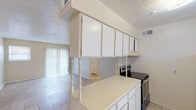 This single-story, 2-bedroom, 1-bathroom unit offers a functional and straightforward layout designed to maximize usability. The living area is bright and open, featuring light-toned tile flooring, neutral cream-colored walls, a textured ceiling, and a sliding glass door with vertical blinds that allows natural light to flow in while providing access to the outdoors. A secondary window further enhances the natural lighting in this space.

The kitchen is configured in a galley style and opens toward the living area via a raised breakfast bar supported by a decorative turned post. White cabinetry lines both the upper and lower walls, offering ample storage. Appliances include an electric range and a full-size refrigerator, complemented by a double-basin stainless steel sink positioned beneath a window.

Each bedroom is generously appointed with two reach-in closets fitted with hanging rods, providing substantial storage capacity. The rooms feature the same light tile flooring found throughout the unit, maintaining a cohesive aesthetic.

The bathroom includes a full tub-shower combination with white tile surround, a mirrored medicine cabinet, a single-sink vanity, and a grab bar. Throughout the unit, textured ceilings and neutral finishes create a clean, uniform appearance.