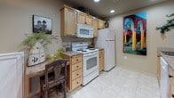 This two-floor residence offers a practical and comfortable layout designed for everyday living. The main level opens into a spacious living area that seamlessly connects the kitchen, dining, and lounge spaces. The kitchen is outfitted with light wood cabinetry, granite-style countertops, tile flooring, and a full suite of white appliances including an electric range, built-in microwave, and refrigerator — providing ample functionality for home cooking. A separate lounge area on the main level features warm neutral tones, plush carpeting, and wall art, creating a relaxed and inviting atmosphere. The upper level hosts the bedrooms, each distinguished by vaulted ceilings that lend an airy, spacious feel. The bedrooms are carpeted and finished in soft earth tones, with natural light entering through windows fitted with blinds. One bedroom includes access to a walk-in closet, adding practical storage. The bathrooms are finished with tile flooring and include a tub-shower combination. Throughout the home, a consistent warm neutral color palette, recessed lighting, and carpeted living spaces contribute to a cohesive, comfortable ambiance suited for residential living.