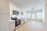 This well-designed 3-bedroom, 2-bathroom unit in Austin, TX offers a clean, modern aesthetic across a single floor. The open-concept kitchen and living area form the heart of the home, featuring stainless steel appliances — including an electric range, built-in microwave, and dishwasher — paired with two-tone cabinetry in white and light wood. A white subway tile backsplash adds a contemporary touch, while light wood-look flooring flows seamlessly throughout the space. The living area is bright and airy, with large windows and a glass door that flood the space with natural light and lead to an outdoor access point. A ceiling fan overhead enhances comfort. The bedrooms are well-proportioned, with the generously sized primary bedroom offering a built-in closet with wire shelving and direct access to a bathroom. Secondary bedrooms benefit from large windows with outdoor views of surrounding greenery. The bathrooms are clean and functional, with one featuring a full soaking tub and shower combination with white tile surround. A light-filled hallway connects the private areas of the home. The unit's neutral palette, recessed lighting, and consistent flooring create a cohesive and inviting atmosphere throughout.