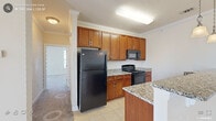 Located at 475 Traebert Circle in Knightdale, NC, this single-floor residence offers a well-organized layout with a thoughtful blend of finishes throughout. The kitchen serves as a functional centerpiece, featuring warm-toned cabinetry with decorative rope detailing, granite countertops, and a full suite of black appliances including a refrigerator, electric range, and over-the-range microwave. A peninsula with matching granite and pendant lighting provides additional prep space and separates the kitchen from the adjoining living area. Light tile flooring runs throughout the kitchen and bathrooms, while crown molding adds a refined touch.

The bedrooms are carpeted and generously proportioned, with large windows that allow natural light to filter in. The primary bedroom is notably well-equipped, offering access to multiple walk-in closets featuring wire shelving systems for organized storage. The bathrooms continue the granite countertop theme, with rich wood-toned vanities, tile flooring, and ample mirror space. The overall interior palette of warm neutrals and cream tones creates a cohesive and inviting ambiance throughout the home.