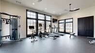 Located at 37 Foxgrove Dr in Dawsonville, Georgia, this dedicated fitness center offers a thoughtfully designed exercise space built to support a full range of workout routines. The single-room layout makes efficient use of its footprint, providing ample open floor space covered in durable, speckled rubber flooring ideal for high-impact activity.

Large, black-framed floor-to-ceiling windows line the main wall, flooding the space with natural light and offering views of the surrounding neighborhood. The bright, neutral-toned walls are complemented by a warm amber accent wall that anchors the strength training zone, adding visual depth and energy to the room. Recessed lighting and a modern ceiling fan with sleek black blades ensure the space remains well-lit and comfortably ventilated during workouts.

The cardio section is outfitted with treadmills, an elliptical, and a stationary bike, all positioned to face the expansive windows. A wall-mounted flat-screen TV is conveniently located nearby. The strength area features a multi-function power rack with weight plates, a dedicated dumbbell rack with a full range of free weights, medicine balls, resistance bands, stability balls, and a adjustable weight bench. Black double doors provide entry and exit access. The overall ambiance is clean, modern, and highly functional.