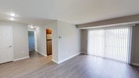 This single-floor residence offers a clean, modern aesthetic throughout its thoughtfully designed layout. The open living area is a standout feature, showcasing smooth laminate wood-look flooring in a warm gray tone and a large sliding glass door dressed with vertical blinds that floods the space with natural light. The living area flows seamlessly toward the kitchen, which is well-equipped with rich warm-toned cabinetry, light granite-style countertops, a stainless steel refrigerator, a gas range, an over-the-range microwave, and a stainless steel sink positioned beneath a window — making it both functional and inviting.

The bedrooms are carpeted in a neutral tone, providing comfort underfoot. Each room is generously sized with natural light from windows fitted with blinds, and the primary bedroom features dual closets, including a wide reach-in closet with built-in shelving and hanging rods, offering excellent storage capacity.

The bathroom is finished with clean white tile surrounding the tub-shower combination, complemented by brushed nickel fixtures and accessories, light tile flooring, and a vanity with a countertop sink. The overall palette throughout the residence — soft grays, whites, and warm wood tones — creates a cohesive, move-in-ready atmosphere that is both practical and visually appealing.