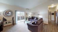 Located at 2112 Meridian Ave E in Edgewood, Washington, this single-floor residence offers a well-organized and comfortable layout designed for everyday living. The living room is a welcoming space featuring neutral-toned carpet, a wall-mounted flat-screen TV with a fireplace console, and a glass-top coffee table. A wall-mounted mini-split system provides climate control, while large sliding glass doors open to a private balcony, filling the room with natural light and providing views of the surrounding community. The dining area is defined by a glass-top table set for four beneath a brushed nickel chandelier, complemented by a wall-mounted TV and contemporary artwork. The galley-style kitchen is equipped with stainless steel appliances, including a refrigerator, range, and microwave, alongside warm wood cabinetry, light countertops, a double stainless sink, and durable hardwood-style flooring. The space includes two carpeted bedrooms, each with windows overlooking the neighborhood, providing ample natural light and storage. The full bathroom features a double-sink vanity with wood cabinetry, a large mirror with overhead lighting, tile flooring, and a shower-tub combination, offering both functionality and comfort throughout.
