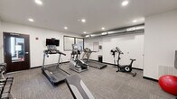 Located at 719 Virginia Ave in Indianapolis, IN, this fitness center offers a well-equipped exercise room designed to support a well-rounded workout routine. The space features a clean, modern aesthetic with crisp white walls, recessed lighting, and durable carpet tile flooring that provides both comfort and traction underfoot. Exposed ductwork along the ceiling adds an industrial touch to the otherwise streamlined interior.

The room is outfitted with a comprehensive selection of cardio equipment, including multiple treadmills from True and Spirit, an elliptical trainer, and a stationary bike, giving users a variety of options for cardiovascular exercise. A wall-mounted flat-screen television accompanies the cardio machines, enhancing the workout experience. For strength training, the space includes a rack of dumbbells in graduated weights, a adjustable workout bench, wall-mounted pull-up bars, and a stability ball with weight plates. A large wall mirror expands the visual depth of the room and assists with form checks during exercise.

A posted fitness area rules sign keeps the environment organized and user-friendly. The room benefits from recessed ceiling lights that ensure consistent, bright illumination throughout. The overall ambiance is functional and focused, offering residents or guests a practical and well-maintained space to maintain their fitness routines.