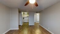 This single-floor unit is designed with a practical, open layout that connects the main living areas seamlessly. The living room is a comfortable, open space finished with warm wood-look flooring and neutral gray walls, with a ceiling fan providing both light and airflow. A textured popcorn ceiling is consistent throughout the unit. The living area flows naturally toward the kitchen, which is separated by a partial wall divider, creating a semi-open feel while maintaining functional distinction between spaces.

The kitchen is efficiently arranged along a single wall, featuring cream-toned cabinetry, a stainless steel sink with a modern faucet, a countertop range, and ample upper and lower cabinet storage. Recessed under-cabinet lighting adds functionality to the workspace.

The bedroom is carpeted for comfort and includes a ceiling fan, as well as a sliding glass door that opens to an outdoor balcony, allowing natural light to filter in and providing an outdoor view. White vertical blinds offer privacy when needed.

The bathroom features a vanity with white cabinetry, light countertops, and a wall-mounted mirror, alongside a separate wet area housing a tiled bathtub and toilet. Wood-look flooring extends through the bathroom, maintaining visual consistency with the rest of the unit.