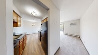 This 1-bedroom, 1-bathroom unit offers a thoughtfully arranged single-floor layout that maximizes functionality and comfort. The open-concept living and dining area is anchored by plush carpeting, baseboard heating, and a wall-mounted air conditioning unit. A sliding glass door fills the space with natural light and opens to a private balcony overlooking a scenic, tree-lined exterior — a standout feature of the living area.

The galley-style kitchen is efficiently designed with warm oak cabinetry, dark granite-style countertops, a stainless steel double sink, and a full suite of black appliances including a refrigerator, electric range, and dishwasher. Wood-look flooring runs throughout the kitchen, which connects seamlessly to the hallway and remaining rooms.

The bedroom offers a comfortable footprint with soft carpeting, a large closet with sliding panel doors, and a window that frames natural views and brings in ample daylight. Baseboard heating ensures year-round comfort.

The bathroom is clean and well-appointed, featuring a full tub/shower combination with white tile surround, mosaic tile flooring, a dark-toned vanity with a white countertop, and a blue-gray accent wall that adds a touch of modern style. A connecting hallway ties all rooms together, providing an efficient and logical flow throughout the unit.