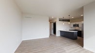 This well-designed single-floor unit showcases a clean, contemporary aesthetic throughout. The open-concept living and kitchen area is anchored by light-toned luxury vinyl plank flooring, crisp white walls, and recessed lighting. A sliding barn door adds a modern touch and connects the living space to the rest of the unit.

The kitchen is a standout feature, equipped with a large dark-paneled island topped with white countertops and an integrated sink. White upper cabinetry, subway tile backsplash, and a full suite of stainless steel appliances—including a refrigerator, range, and over-the-range microwave—complete the functional and stylish space. Pendant lighting above the island adds warmth and visual interest.

The spacious living area offers ample room for flexible furniture arrangements, benefiting from an open layout and a neutral color palette that creates a bright, airy ambiance.

The bathroom is finished with large-format, light-toned tile on both the floors and walls, a glass-enclosed walk-in shower with a built-in bench, and a dark-toned vanity with a backlit mirror.

The bedroom features plush carpeting and a generously sized reach-in closet with wire shelving and hanging rods, providing practical and organized storage. Overall, the unit presents a cohesive modern design with quality finishes throughout.
