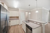 This well-appointed 1,320 sq ft single-story residence in Holly Springs, NC offers 3 bedrooms and 2 bathrooms across an efficiently designed floor plan. The open-concept kitchen and living area serves as the heart of the home, featuring warm hardwood-style flooring, crown molding, and ceiling fans throughout. The kitchen is equipped with cream cabinetry, granite countertops, stainless steel appliances including a refrigerator, range, and over-the-range microwave, and a peninsula island with pendant lighting. The spacious living room benefits from abundant natural light through large multi-pane windows and direct access to the outdoors. The 160 sq ft primary bedroom includes plush carpeting, a ceiling fan, and a closet with built-in wire shelving and hanging rods. Additional bedrooms are carpeted and feature natural light from large windows. The bathrooms showcase hardwood-style flooring, white cabinetry with granite countertops, and natural light. A dedicated laundry room includes overhead cabinetry and full-size washer and dryer hookups. Three hallways connect the space efficiently, completing this functional and comfortable home.