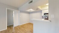 This single-floor, one-bedroom, one-bathroom unit offers a well-organized layout designed to maximize functionality within a compact footprint. The living area features light gray laminate wood flooring, neutral-toned walls, and a notable skylight that introduces natural light from above, creating an open and airy atmosphere. Vertical blinds on a sliding glass door provide additional light control and outdoor access.

The galley-style kitchen is efficiently arranged with white cabinetry, light stone countertops, a subway tile backsplash, stainless steel appliances including a refrigerator, range, microwave, and dishwasher, and a double-basin sink. A peninsula counter separates the kitchen from the living area, offering a practical transition between spaces.

The bedroom is carpeted for comfort, features neutral walls, and includes a window fitted with horizontal blinds that allow natural light while maintaining privacy. A dedicated closet provides storage within the room.

The bathroom is clean and straightforward, featuring wood-look tile flooring, a tub-shower combo with white tile surround, and a toilet. A hallway connects the primary spaces, with a closet providing additional storage. The entrance leads directly into the main living area, establishing a logical and easy-to-navigate floor plan throughout.