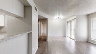 This well-appointed single-floor unit offers an efficient layout across a comfortable footprint, combining practical design with notable finishing details. The open living room serves as the central gathering space, distinguished by a full-height brick fireplace with a raised hearth that anchors the room as a focal point. Sliding glass doors admit natural light and provide access to an outdoor area, complemented by additional windows fitted with blinds. A textured popcorn ceiling and a multi-bulb light fixture complete the living area's character.

The kitchen is thoughtfully arranged in a galley configuration, featuring white shaker cabinetry with matte black hardware, light granite countertops, a stainless steel sink, and a full suite of stainless steel appliances including a refrigerator, range, microwave, and dishwasher. Wood-look plank flooring runs through the main living areas and kitchen, while a hallway with a closet connects to the private quarters.

The bedroom is carpeted for comfort and includes a ceiling fan, a sliding glass door to an outdoor space, and a dedicated closet. The bathroom presents white cabinetry, granite countertops with matte black fixtures, and wood-look flooring, maintaining a cohesive, updated aesthetic throughout the unit.