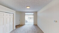 Located in Indianapolis, IN, this single-story residence offers a clean, functional layout with a neutral color palette and consistent finishes throughout. The living area greets occupants at the entry, where a sliding glass door with vertical blinds and a transom window above allow natural light to fill the carpeted space, creating a bright and open atmosphere.

The kitchen is positioned in an open-concept arrangement adjacent to the living area, defined by a peninsula counter finished with light granite-patterned laminate and a stainless steel sink. White cabinetry lines the kitchen walls, complemented by black appliances including a refrigerator and range. Tile flooring in the kitchen transitions to plush carpet in the adjoining living and bedroom areas. A large double-door closet is conveniently located near the kitchen.

The bedroom features soft carpeting underfoot, a ceiling fan with integrated lighting, and a window fitted with blinds that provides natural light. The bathroom is well-appointed with a single-sink vanity topped with a white countertop, ample cabinet storage below, a wide wall mirror with a lighted bar above, and a full tub and shower combination with tile surround. Textured ceilings are consistent throughout the space, contributing to its straightforward, practical character.