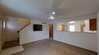 This multi-story home is spread across three floors, offering a versatile and functional layout suited for a variety of lifestyles. The main living area is finished with wall-to-wall carpeting that adds warmth and comfort underfoot. A ceiling fan with integrated lighting serves as a central fixture in the living room, providing both airflow and ambient illumination. A wall-mounted television mount is already in place, making the space immediately media-ready. One of the standout architectural details is the open pass-through window connecting the living area to the kitchen, promoting a sense of openness and easy communication between spaces. The kitchen area, visible through the pass-through, benefits from natural light provided by a window. Neutral white walls throughout create a clean, bright canvas that complements a wide range of décor styles. A staircase is conveniently located within the living space, providing access to the additional floors of the home. Doorways lead to further rooms, hinting at a well-connected floor plan. The consistent use of warm wood-toned trim and transitions adds a cohesive finishing touch throughout. The overall ambiance is light, neutral, and move-in ready.
