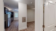 This single-floor unit offers a thoughtfully designed open-concept layout that seamlessly connects the kitchen and living areas. The kitchen is a standout feature, showcasing bold dark cabinetry contrasted by granite countertops, a stainless steel undermount sink, and a full suite of stainless steel appliances including a refrigerator, electric range, over-the-range microwave, and dishwasher. Light wood-style flooring runs throughout the main living areas, lending warmth and continuity to the space. The living area is bathed in natural light from multiple windows fitted with white blinds, and a ceiling fan adds both comfort and style. A door with transom window provides additional brightness and access to the exterior. The bathroom is efficiently laid out, featuring dark wood vanity cabinetry topped with granite, a single sink, a full tub-shower combination with chrome fixtures, and matching wood-style flooring. A carpeted room off the main hallway provides a quiet, comfortable retreat. A utility area with an accessible electrical panel is also present, adding practical functionality. Throughout the space, neutral wall tones and clean white trim create a bright, modern ambiance.