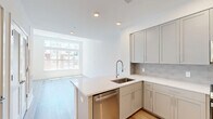 This thoughtfully designed 2-bedroom, 1-bathroom residence offers a clean, contemporary aesthetic across a single floor. Light-toned hardwood flooring flows consistently throughout the space, complementing the crisp white walls and creating a bright, cohesive atmosphere.

The kitchen is a standout feature, showcasing gray shaker-style cabinetry, white quartz countertops, a subway tile backsplash, and a full suite of stainless steel appliances including a gas range, built-in microwave, and french door refrigerator. A peninsula with seating overhang connects the kitchen to the open living area, maximizing functionality. Recessed lighting illuminates the space efficiently.

Both bedrooms benefit from large, floor-to-ceiling windows that invite abundant natural light and offer views of the surrounding neighborhood. The primary bedroom is generously sized, while the second bedroom also features a sizable window with similar urban views. A hallway with light hardwood flooring connects the bedrooms to the shared full bathroom, which includes a soaking tub/shower combination, toilet, and vanity with tile flooring. A dedicated closet provides additional storage. The overall design is clean, modern, and move-in ready.
