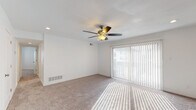 This single-floor residence offers a thoughtfully designed layout with a neutral, clean aesthetic throughout. The spacious living area is a standout feature, centered around a ceiling fan with a light fixture and recessed lighting. Large sliding glass doors dressed with vertical blinds invite an abundance of natural light, casting bright patterns across the plush carpeted floors and creating an open, airy ambiance. The entry area transitions seamlessly from hard flooring into the carpeted living space.

The kitchen is well-equipped and stylish, featuring gray shaker-style cabinetry, granite-look countertops, a white subway tile backsplash, and wood-look flooring. Black appliances — including an electric range, over-the-range microwave, and dishwasher — complement the double-basin sink with a modern faucet, making this a fully functional cooking space.

The bedrooms are generously proportioned with soft carpeting and windows that provide natural light. One bedroom features dual closets with ample built-in shelving, offering excellent storage capacity. The bathroom is clean and bright, with white subway tile surrounding a full soaking tub and shower combo, accented by chrome fixtures and wood-look flooring. The overall design is cohesive, practical, and move-in ready.