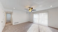 This single-floor residence offers a thoughtfully designed layout with a neutral, clean aesthetic throughout. The spacious living area is a standout feature, centered around a ceiling fan with a light fixture and recessed lighting. Large sliding glass doors dressed with vertical blinds invite an abundance of natural light, casting bright patterns across the plush carpeted floors and creating an open, airy ambiance. The entry area transitions seamlessly from hard flooring into the carpeted living space.

The kitchen is well-equipped and stylish, featuring gray shaker-style cabinetry, granite-look countertops, a white subway tile backsplash, and wood-look flooring. Black appliances — including an electric range, over-the-range microwave, and dishwasher — complement the double-basin sink with a modern faucet, making this a fully functional cooking space.

The bedrooms are generously proportioned with soft carpeting and windows that provide natural light. One bedroom features dual closets with ample built-in shelving, offering excellent storage capacity. The bathroom is clean and bright, with white subway tile surrounding a full soaking tub and shower combo, accented by chrome fixtures and wood-look flooring. The overall design is cohesive, practical, and move-in ready.
